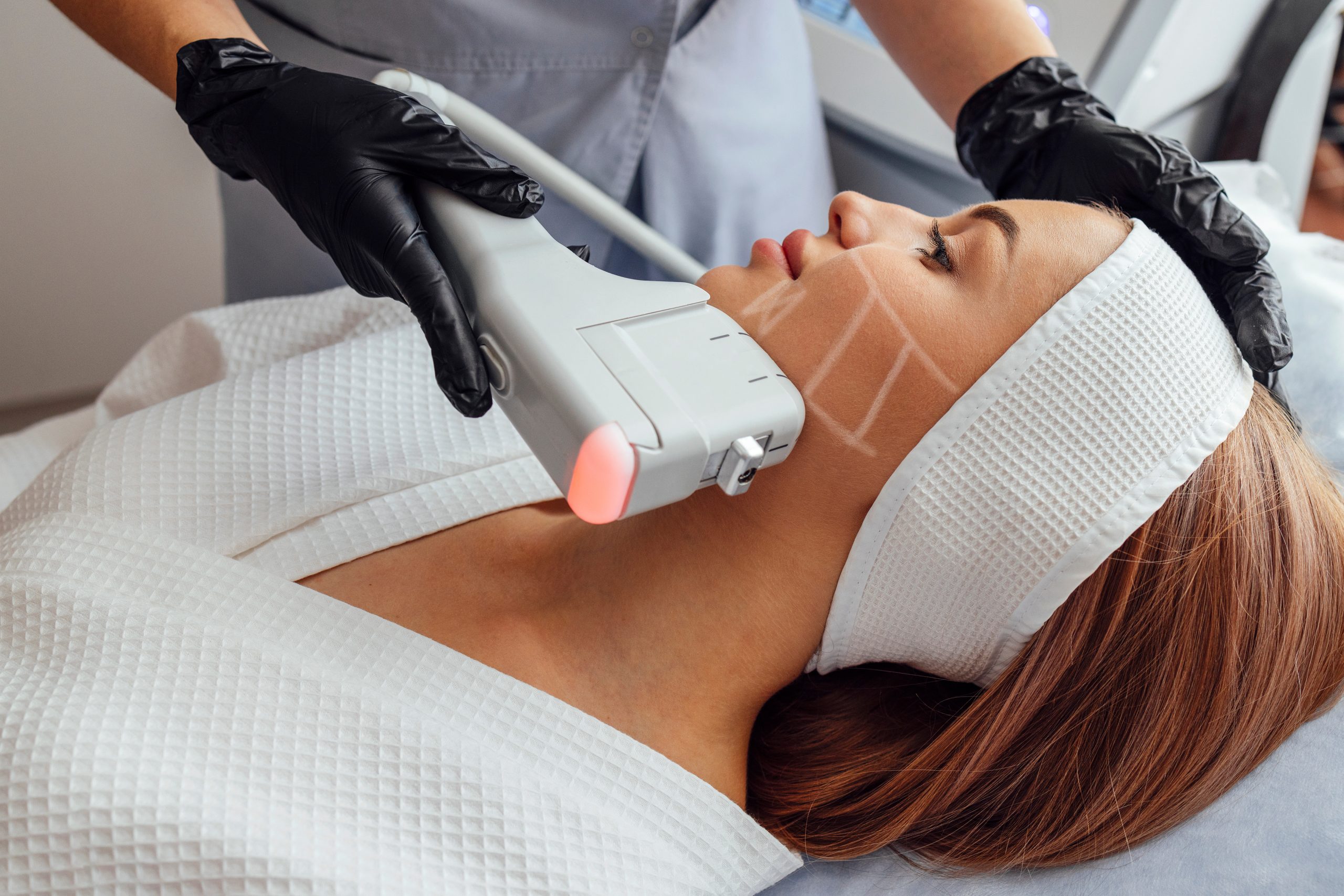 Portrait of relaxed young female client getting SMAS ultrasound face lifting massage with professional equipment in beauty center